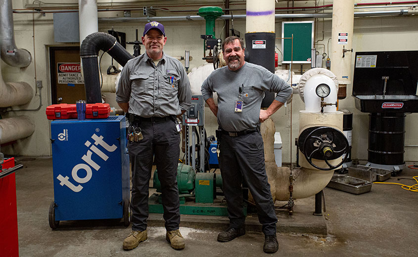 Two men standing in front of pipes and equipment