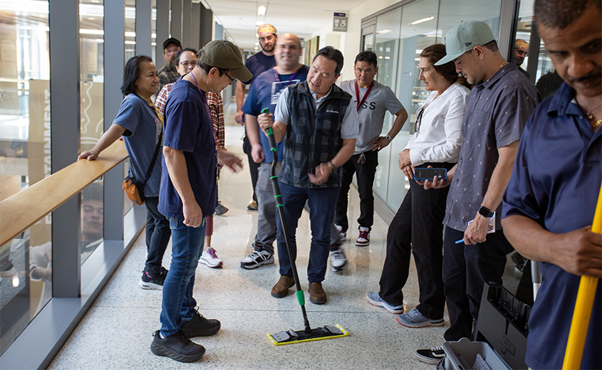 man shows a group of people a mop in a hallway