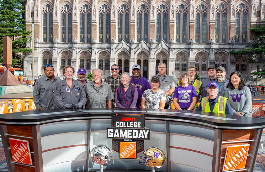 people lined up behind College GameDay desk with Suzzallo Library in the background