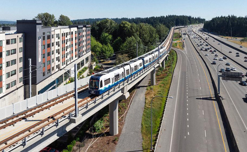 Sound Transit train on elevated track with trees and building in the background