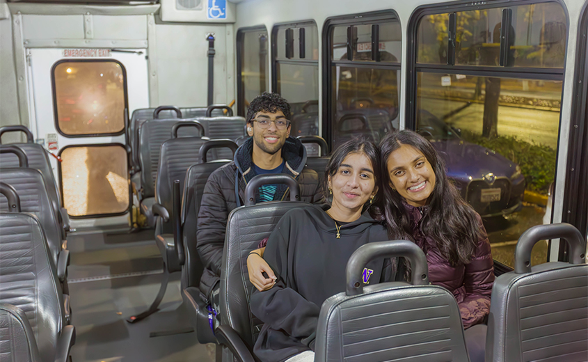 three students smile while sitting in a shuttle