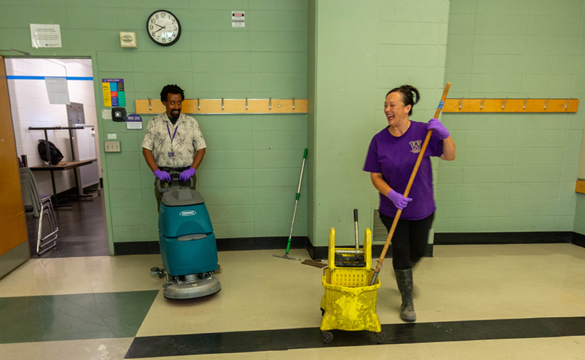 woman smiling as she mops and man with cleaning machine