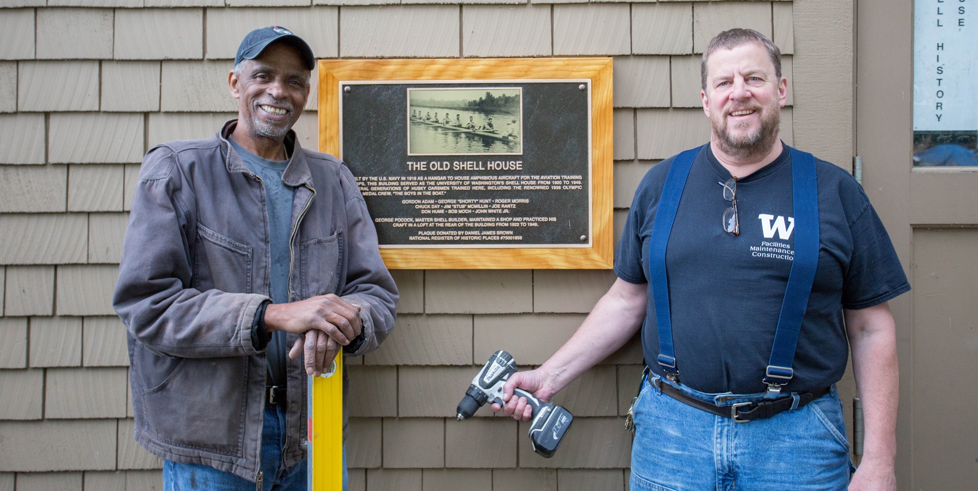 Two UW carpenters stand with a plaque on the Canoe House