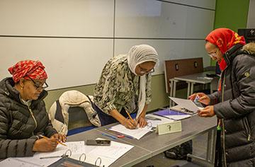 Two women work together on a class activity while another woman sits nearby