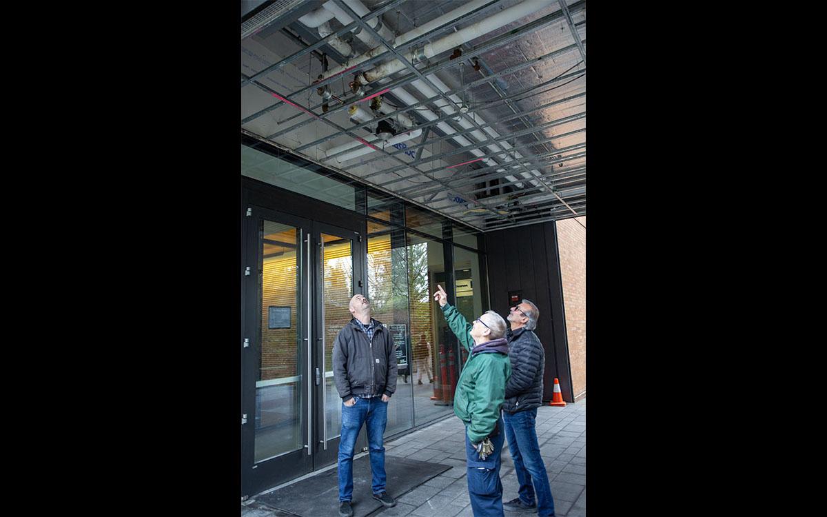 three people looking up at exposed cracked pipe in ceiling of breezeway