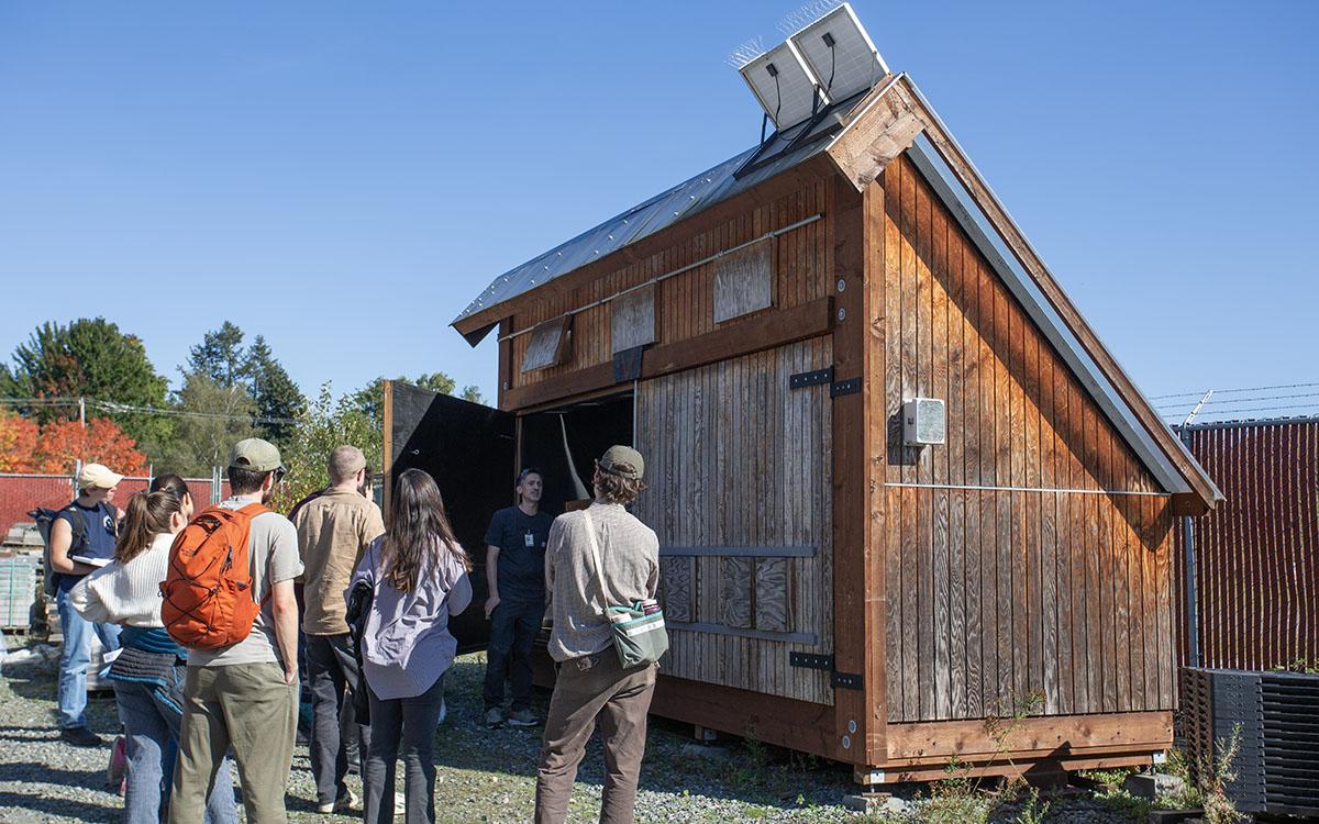 students gather around small building that slopes on one side