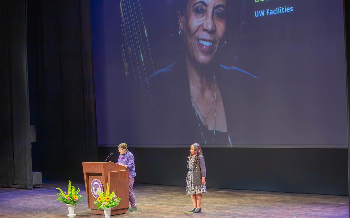 President Cauce talks at podium on stage, Leula Amaha stands nearby