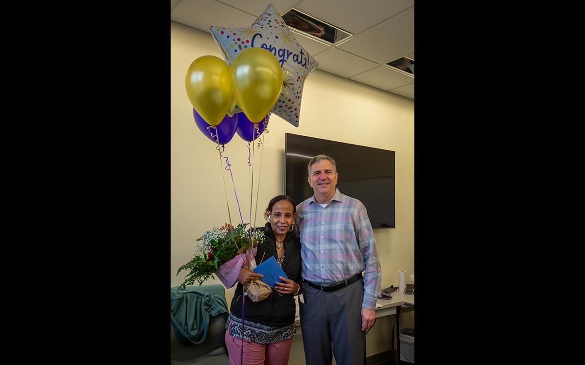 Interim Vice President of Facilities stands with Leula Amaha, who is holding balloons and flowers