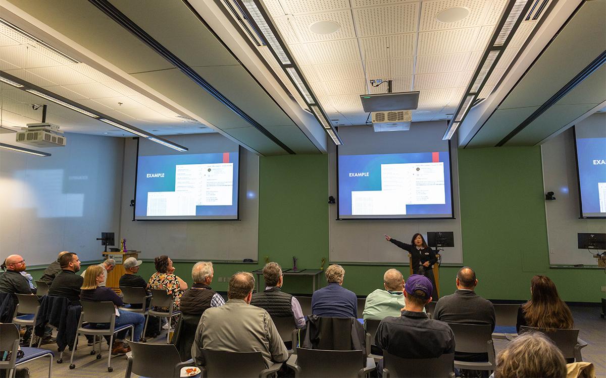 woman speaking in front of a room with arms outstretched