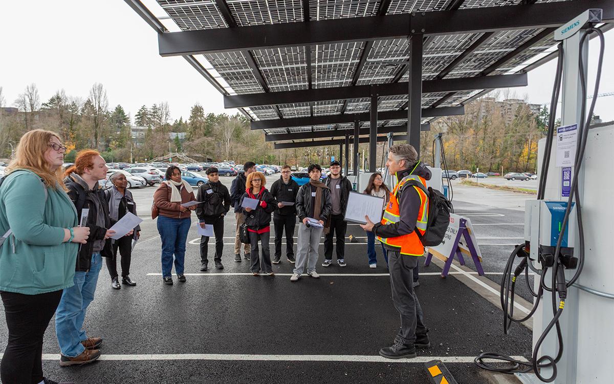 person speaking to small crowd underneath solar canopy