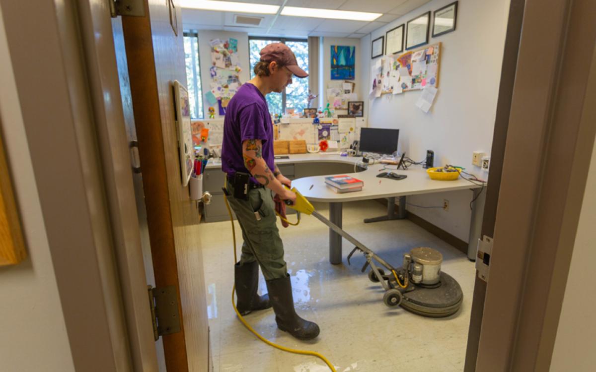 man using machine to strip wax from floor of office