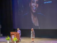 President Cauce talks at podium on stage, Leula Amaha stands nearby