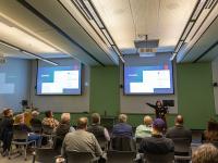 woman speaking in front of a room with arms outstretched