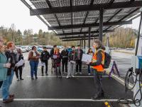 person speaking to small crowd underneath solar canopy