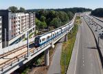 light rail train on elevated track with trees and buildings in the background