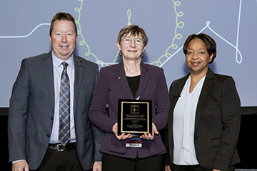 Woman holding award standing between two other people
