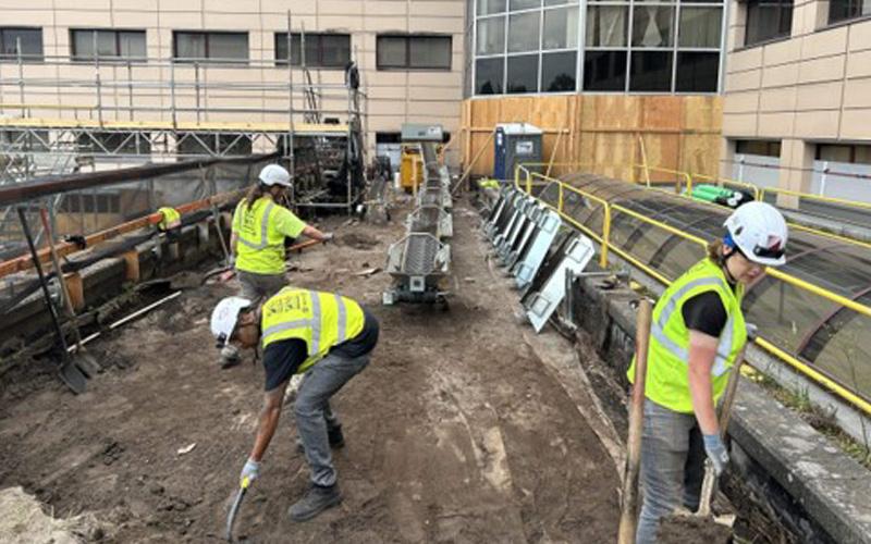 three construction workers on a third floor roof shoveling off old material