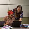 woman helps another woman, who is working on the computer