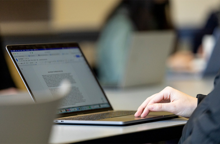 a person's hand on a Macbook looking at an essay on the screen