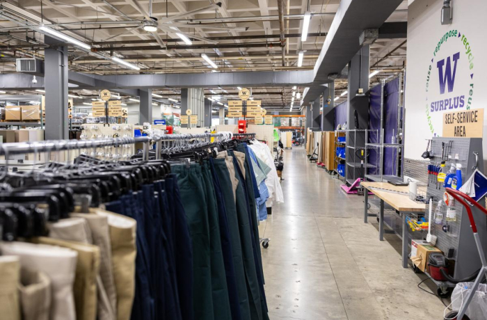 a rack of cloths with other items behind; a wall that says uw surplus on the right