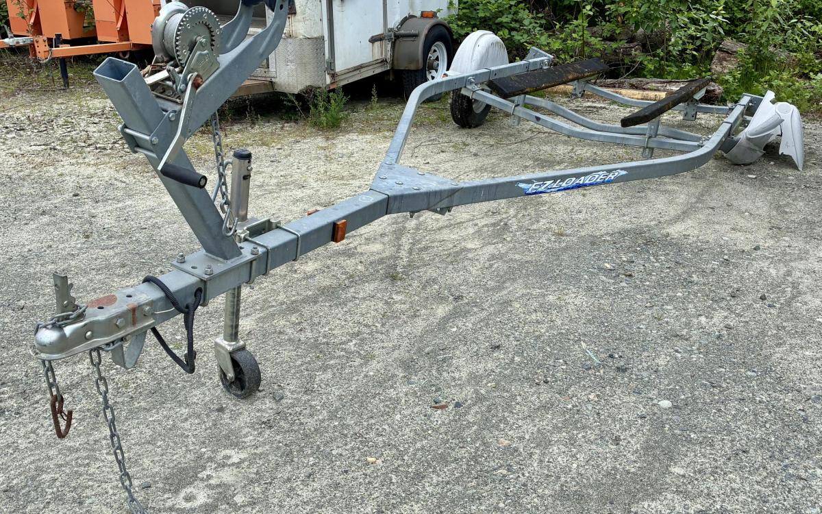 A boat trailer missing one wheel in a gravel parking lot.