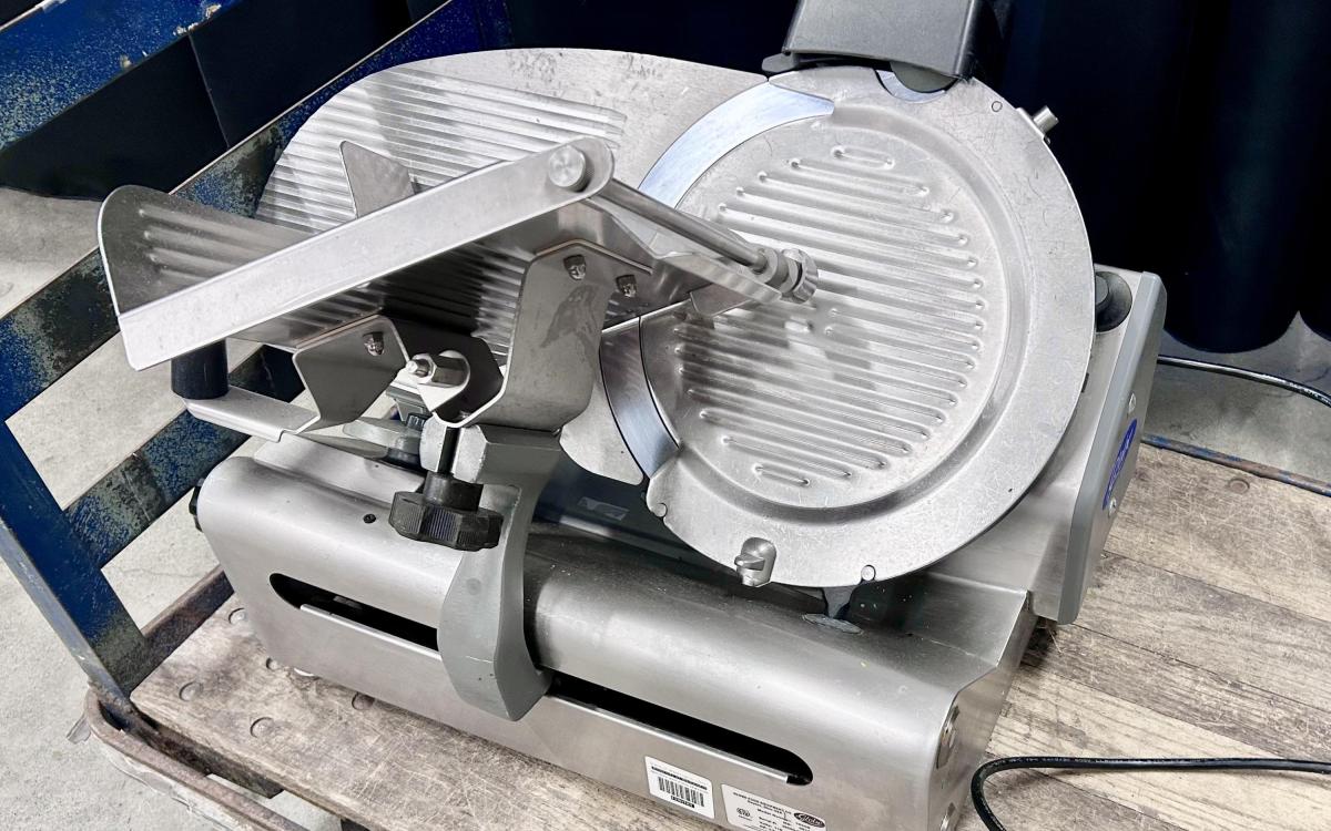 Metal commercial deli slicer on a cart.