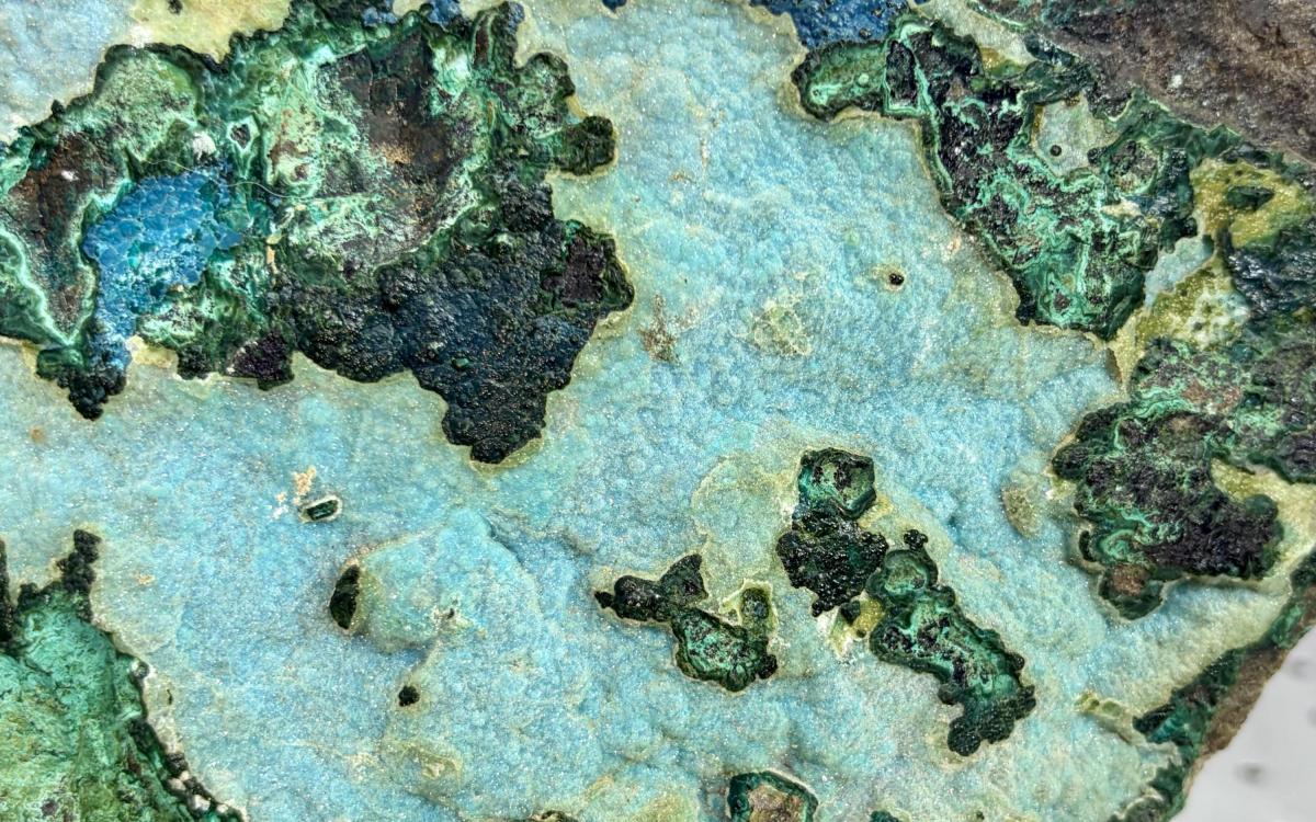 Close up of a rock with mulitiple areas of green and blue-green minerals viewable.