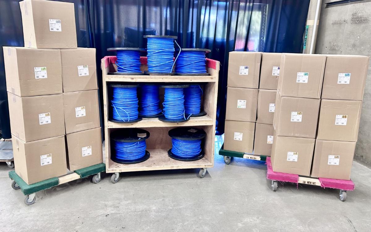 Boxes of Cat-6A cable, with a cart full of spools of the same cable between the stacks of boxes.