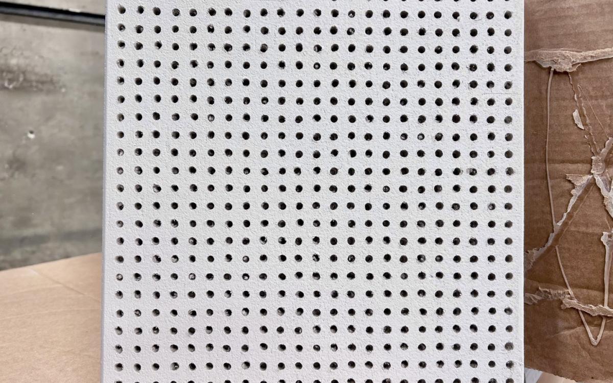 A sample perforated acoustical tile sits on boxes. 