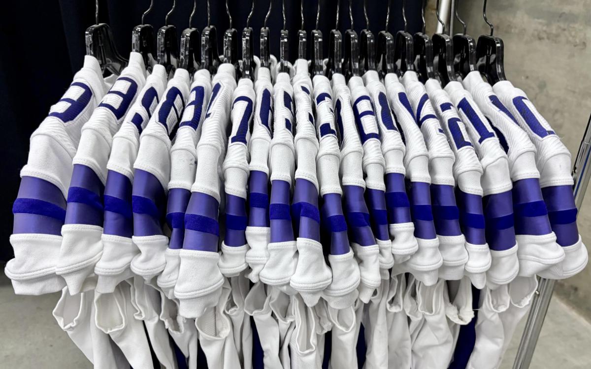Twenty white and purple football jerseys hang on hangers.