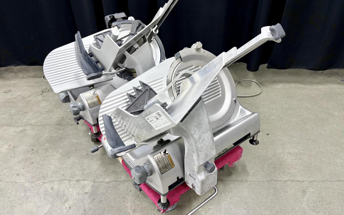 Two similar commercial deli food slicers on a dolly.