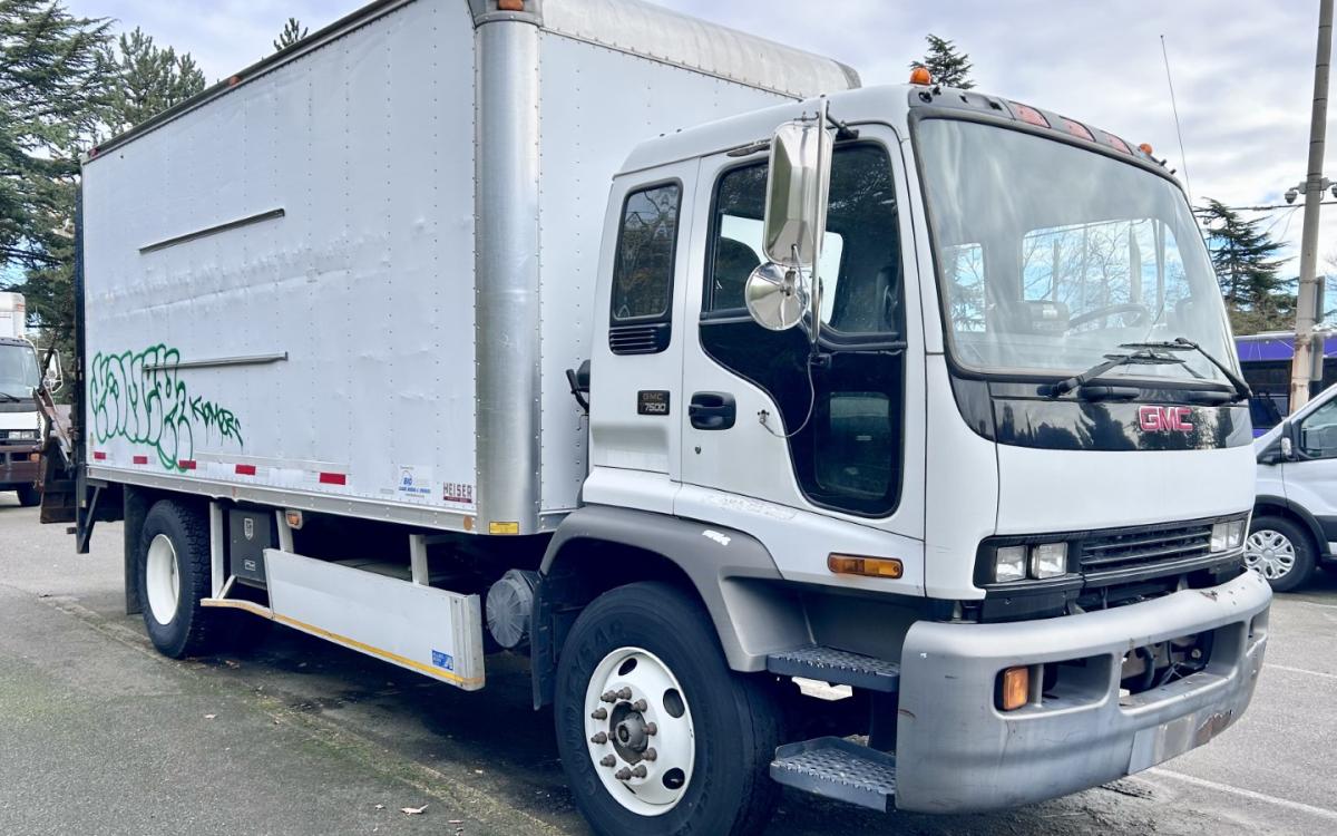 White GMC box truck with graffiti on side in a parking lot.