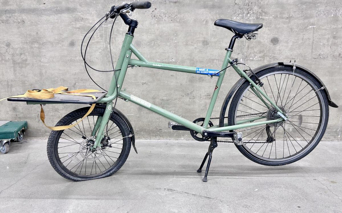 A sage green cargo bike on on its kickstand.