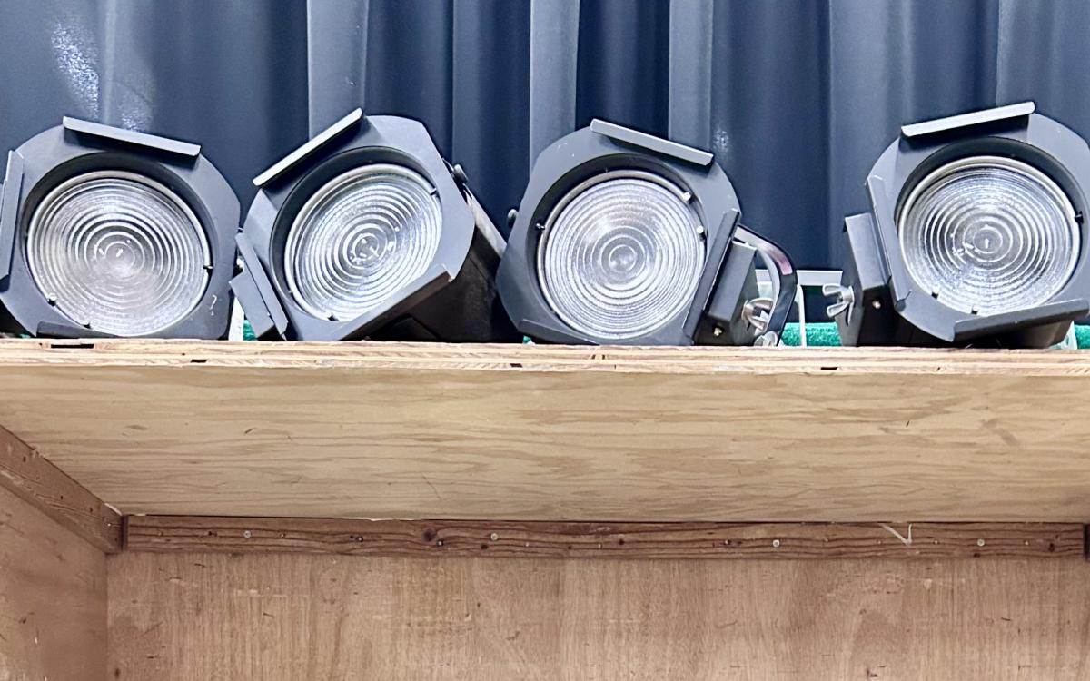 Four fresnel stage lights on a shelf.