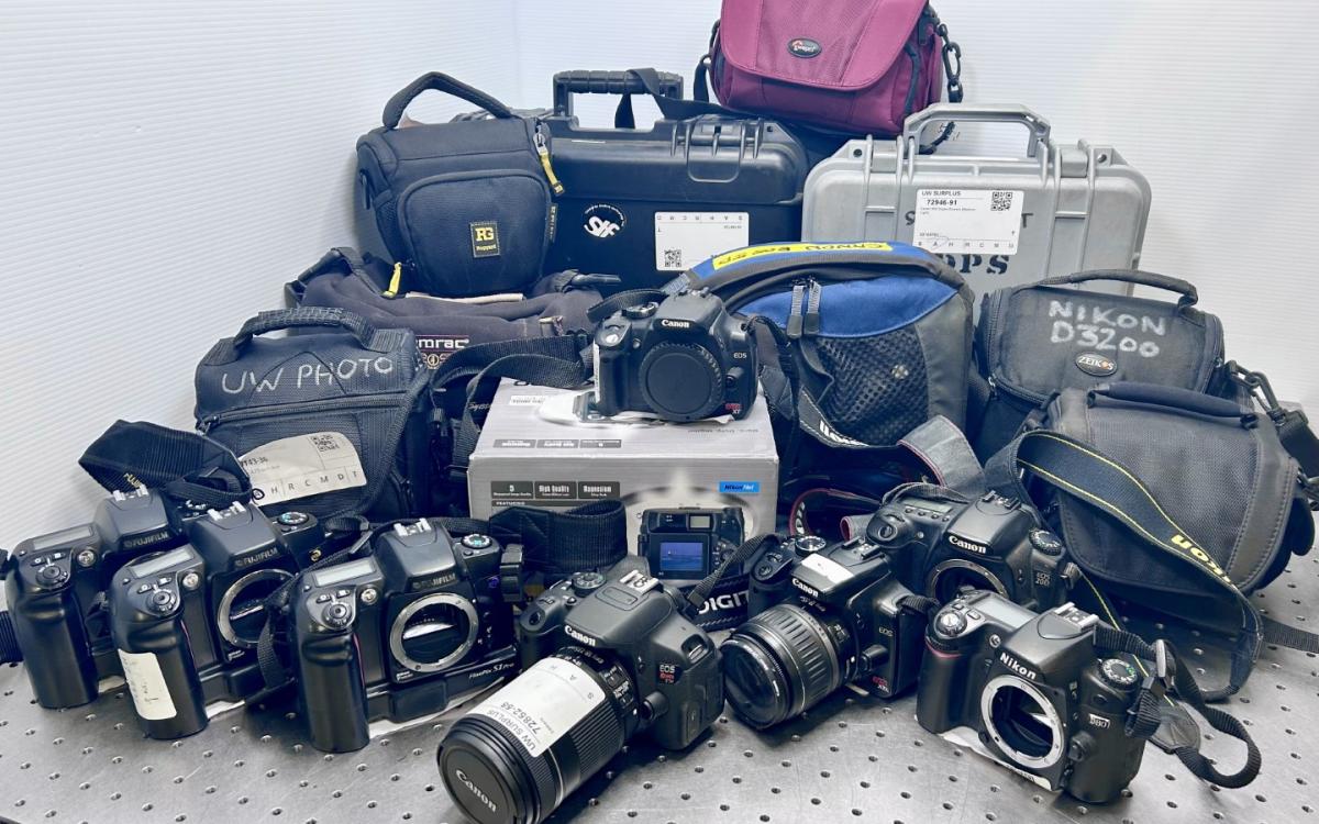 Several various digital cameras, some in cases, displayed on a table.