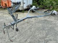 A boat trailer missing one wheel in a gravel parking lot.