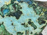Close up of a rock with mulitiple areas of green and blue-green minerals viewable.
