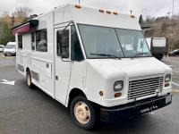 White Truck with food service windows on the side in a parking lot.