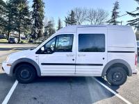 White Ford Transit in a parking lot with trees and blue sky behind.