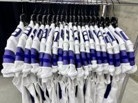 Twenty white and purple football jerseys hang on hangers.