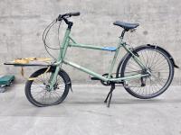 A sage green cargo bike on on its kickstand.