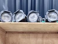 Four fresnel stage lights on a shelf.
