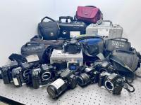 Several various digital cameras, some in cases, displayed on a table.